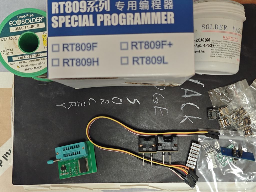 RT809 programmer box with Senju M705 solder wire and Jufeng solder paste on a workbench, with adapters and cables below.